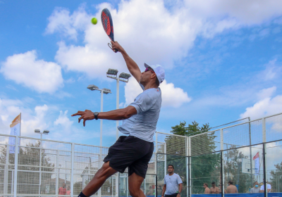 Giocatore di padel in azione, salta con energia sotto un cielo azzurro.