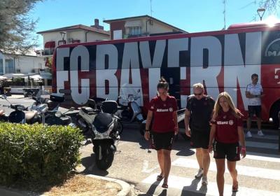 Persone sorridenti davanti a un bus FC Bayern, atmosfera estiva e rilassata.