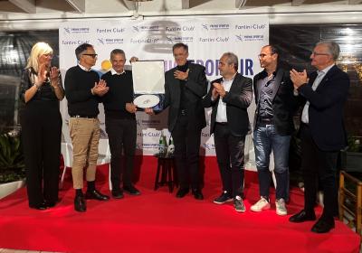 Persone sorridenti applaudono su un palco rosso durante una cerimonia di premiazione.
