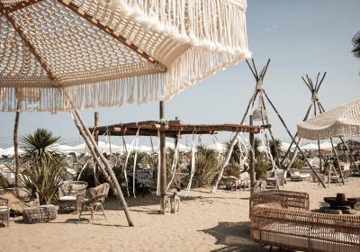 Spiaggia boho-chic con ombrelloni intrecciati e sedie in rattan, atmosfera rilassante e naturale.